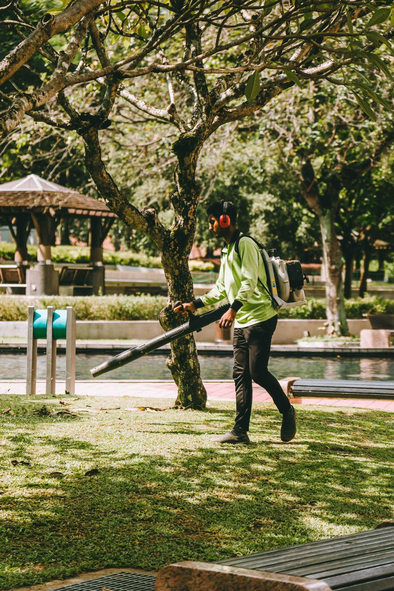 A man using a leaf blower in a vibrant Kuala Lumpur park, showcasing daily outdoor maintenance.