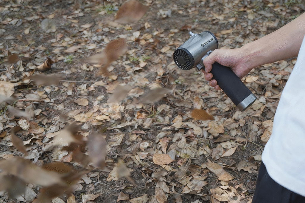 A man uses a handheld cordless leaf blower to blow leaves in a wooded area.